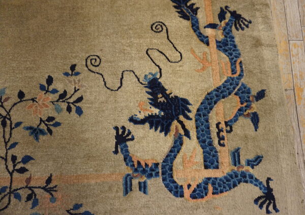 Muted green rug with an ornate blue dragon and peach motifs displayed on light plank flooring.