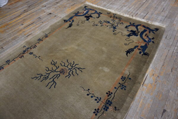 Muted green low-pile rug featuring intricate blue dragon and floral motifs on rustic plank flooring.
