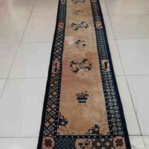 Long tan and dark blue runner rug with detailed patterns, displayed on white tiled floor.