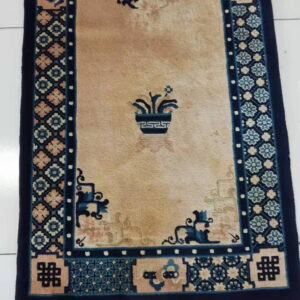 Tan low-pile rug with navy blue, peach, and light blue geometric and floral border designs on a tile floor.