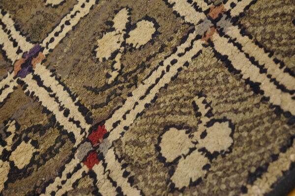 Textured high-pile rug detail showing a beige and dark brown geometric pattern with subtle red and purple accents.
