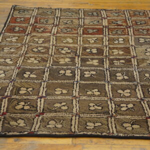 Textured rug with a brown, tan, and red checked pattern featuring beige floral motifs on a wood floor.