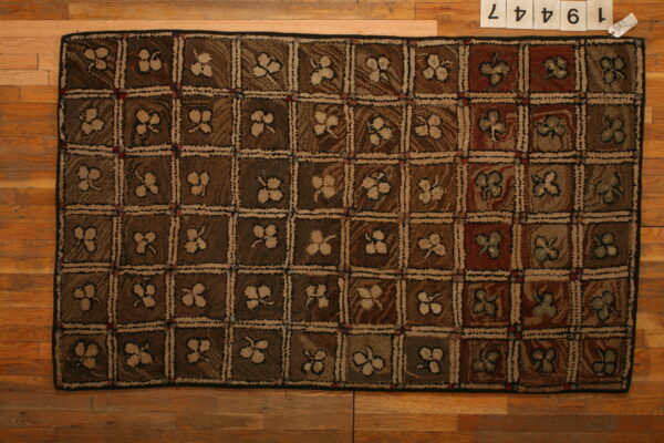 Brown and tan checkerboard rug featuring textured floral squares resting on wood plank flooring.