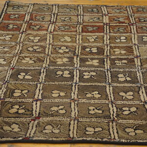 Textured brown and tan rug featuring a square grid pattern with stylized floral motifs on wood planks.