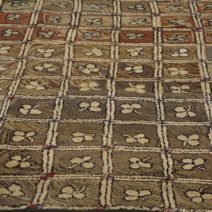 Brown and taupe textured rug with a checkered design and stylized clover motifs on wood floor.