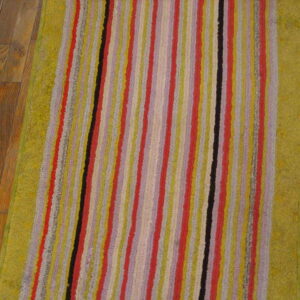 A colorful striped runner with textured lime green borders sits on brown hardwood flooring.