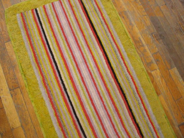 A colorful striped runner rug featuring a wide, textured lime green border rests on wood flooring.