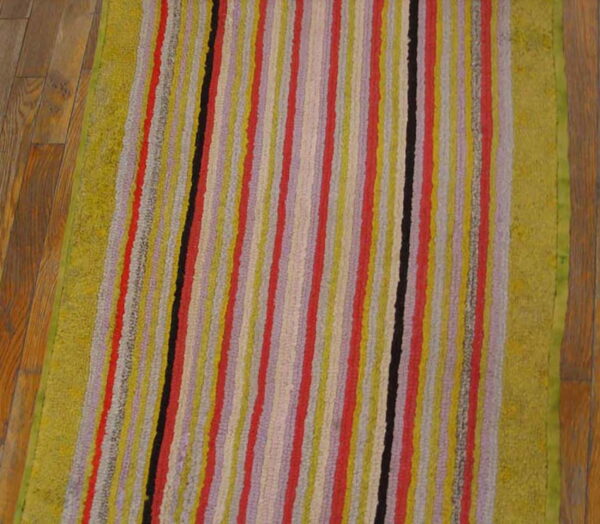 Textured runner rug with multicolor vertical stripes and wide green borders on wood flooring.