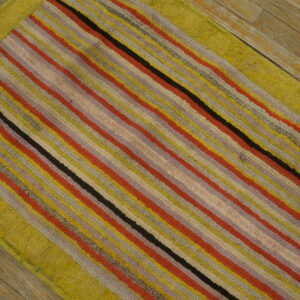 Multi-colored striped rug with a thick chartreuse border on weathered wooden plank flooring.