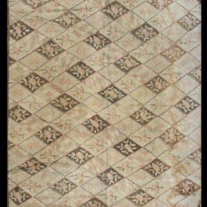 A textured beige rug features a repeating diamond pattern with pink floral motifs on taupe and light backgrounds.