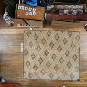 Muted beige rug with a diamond pattern and pink and brown floral designs on hardwood flooring.