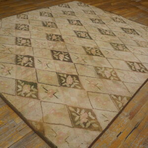 Beige and pink floral rug with a diamond pattern displayed on rustic, wide-plank wood flooring.