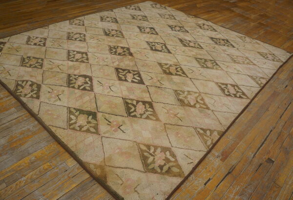 Beige and pink floral rug with a diamond pattern displayed on rustic, wide-plank wood flooring.