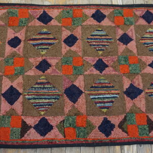 Coarse, looped rug featuring a dense geometric diamond pattern in brown, pink, navy, and orange on wood flooring.