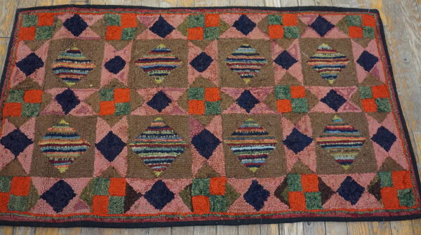 Coarse, looped rug featuring a dense geometric diamond pattern in brown, pink, navy, and orange on wood flooring.