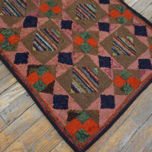 High-pile brown rug with pink, navy, orange, and striped geometric patch squares on distressed wood flooring.