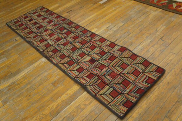 A textured runner features a red and multicolored striped lattice pattern on worn wood floors.