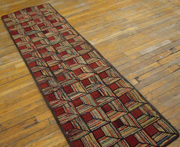 A long, textured runner rug in red and multi-colored striped squares lies on worn wooden planks.