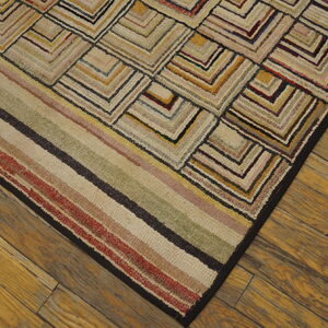 Textured, multicolored rug with angular block patterns and stripes rests on warm, wide wood plank flooring.