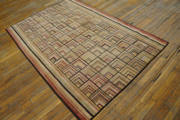 Beige rug with a colorful repeating v-pattern and striped border rests on distressed wood flooring.