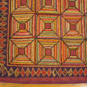 A close-up of a multi-color striped hooked rug featuring geometric blocks and a purple diamond border on wood flooring.