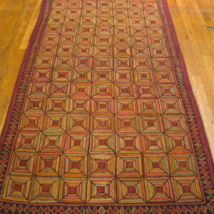 Low-pile runner rug with colorful concentric square motifs on rustic wood planks.