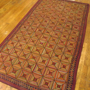 A long, textured rug displays a multicolored striped geometric tumbling cube pattern on worn wood planks.