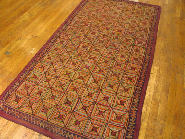 A long, textured rug displays a multicolored striped geometric tumbling cube pattern on worn wood planks.