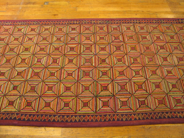 Multicolored hooked rug runner featuring a stacked geometric square pattern on a wood floor.