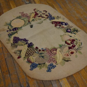 Beige oval hooked rug with a multicolored fruit garland border on rustic wood planks.