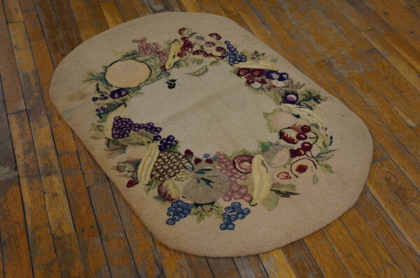 Beige oval hooked rug with a multicolored fruit garland border on rustic wood planks.