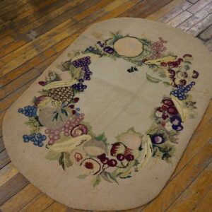 Textured oval beige rug with a colorful fruit garland border resting on distressed hardwood flooring.