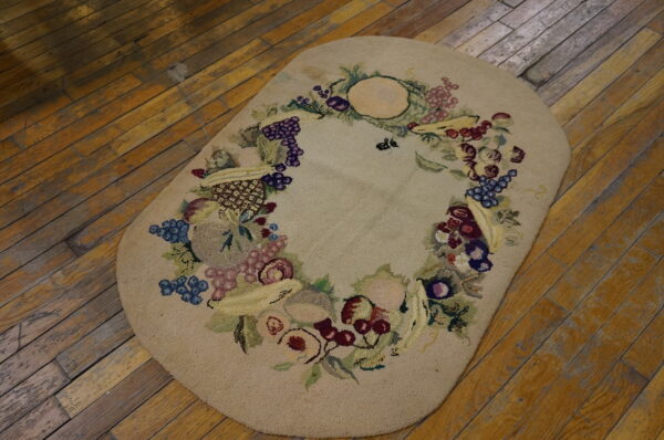 Textured oval beige rug with a colorful fruit garland border resting on distressed hardwood flooring.