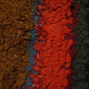 Close-up of a shaggy rug with vertical stripes of brown, blue-gray, red, dark green, and black.