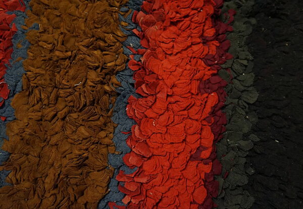 Close-up of a shaggy rug with vertical stripes of brown, blue-gray, red, dark green, and black.