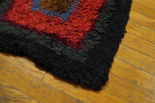 A highly textured, colorful rag rug with geometric blocks of red, black, and blue rests on wood planks.