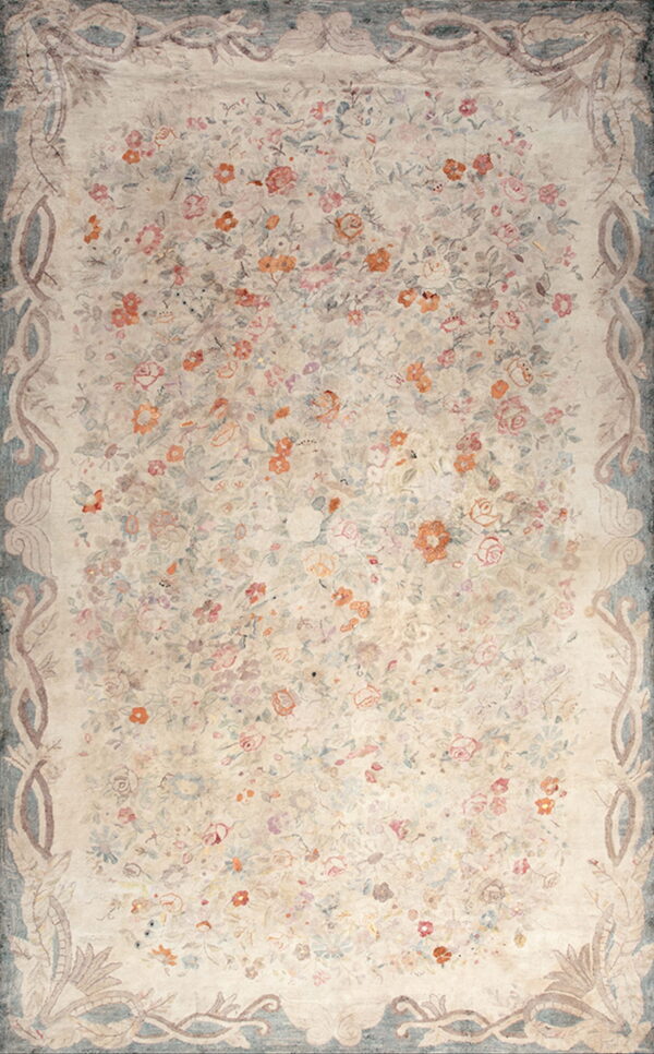 Light beige rug featuring dense pink and terracotta floral motifs and a dusty blue scrolling botanical border.