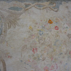 Heavily worn, nubby textured rug featuring a faded tan field, muted floral designs, and a blue decorative border.