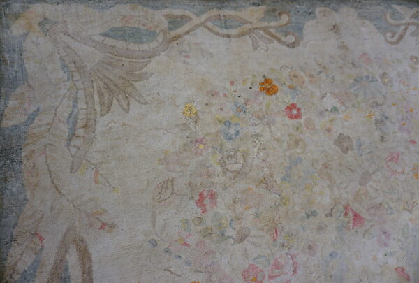 Heavily worn, nubby textured rug featuring a faded tan field, muted floral designs, and a blue decorative border.