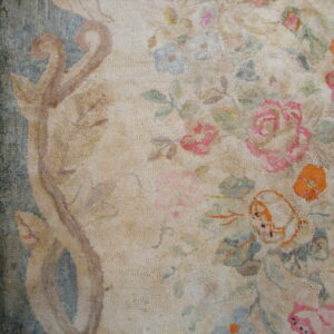 Textured cream rug with faded pink, blue, and orange floral patterns sits beside brown hardwood floors.