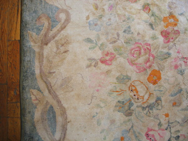 Textured cream rug with faded pink, blue, and orange floral patterns sits beside brown hardwood floors.