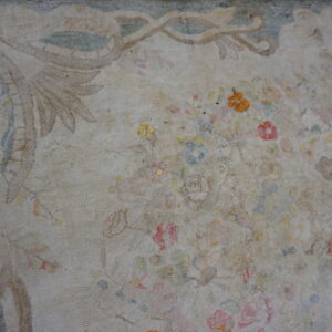 Close-up of a low-pile, distressed rug with a faded beige field, formal border, and scattered pale florals.