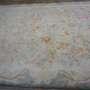 Distressed cream floral rug with pink and yellow faded motifs and a dusty blue border on wood flooring.