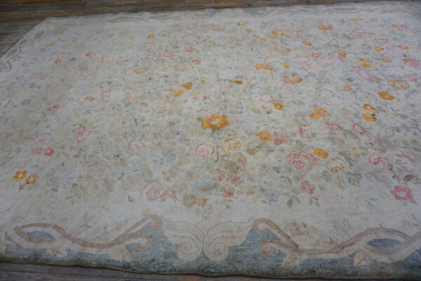 Distressed cream floral rug with pink and yellow faded motifs and a dusty blue border on wood flooring.