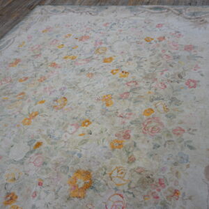 Muted cream rug featuring a dense floral pattern in pink, yellow, and blue on dark wood planks.