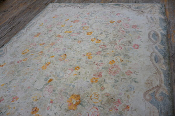 Muted cream rug featuring a dense floral pattern in pink, yellow, and blue on dark wood planks.