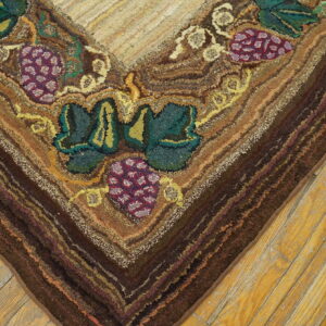 Textured rug corner with grapes and leaves in green, purple, and brown tones rests on worn wood planks.