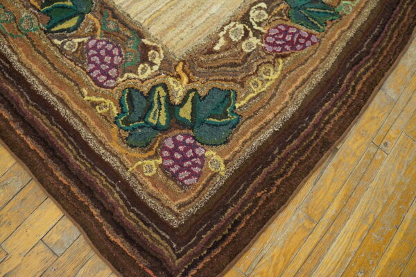 Textured rug corner with grapes and leaves in green, purple, and brown tones rests on worn wood planks.