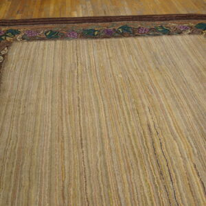 A textured beige and gold striped rug featuring a dark brown grape and leaf border on a wood floor.