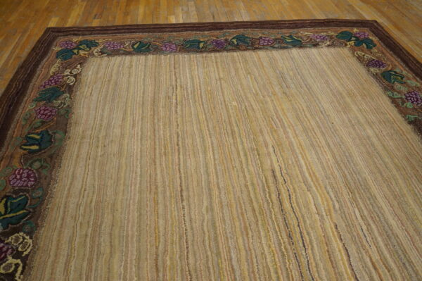 A textured beige and gold striped rug featuring a dark brown grape and leaf border on a wood floor.